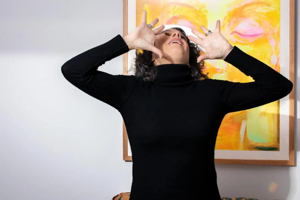 Jodee Blanco striking an expressive pose in front of a colorful painting